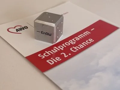 Kleiner Aluminiumwürfel mit EnBW-Logo auf einer Broschüre zum Schulprogramm „Die 2. Chance“.